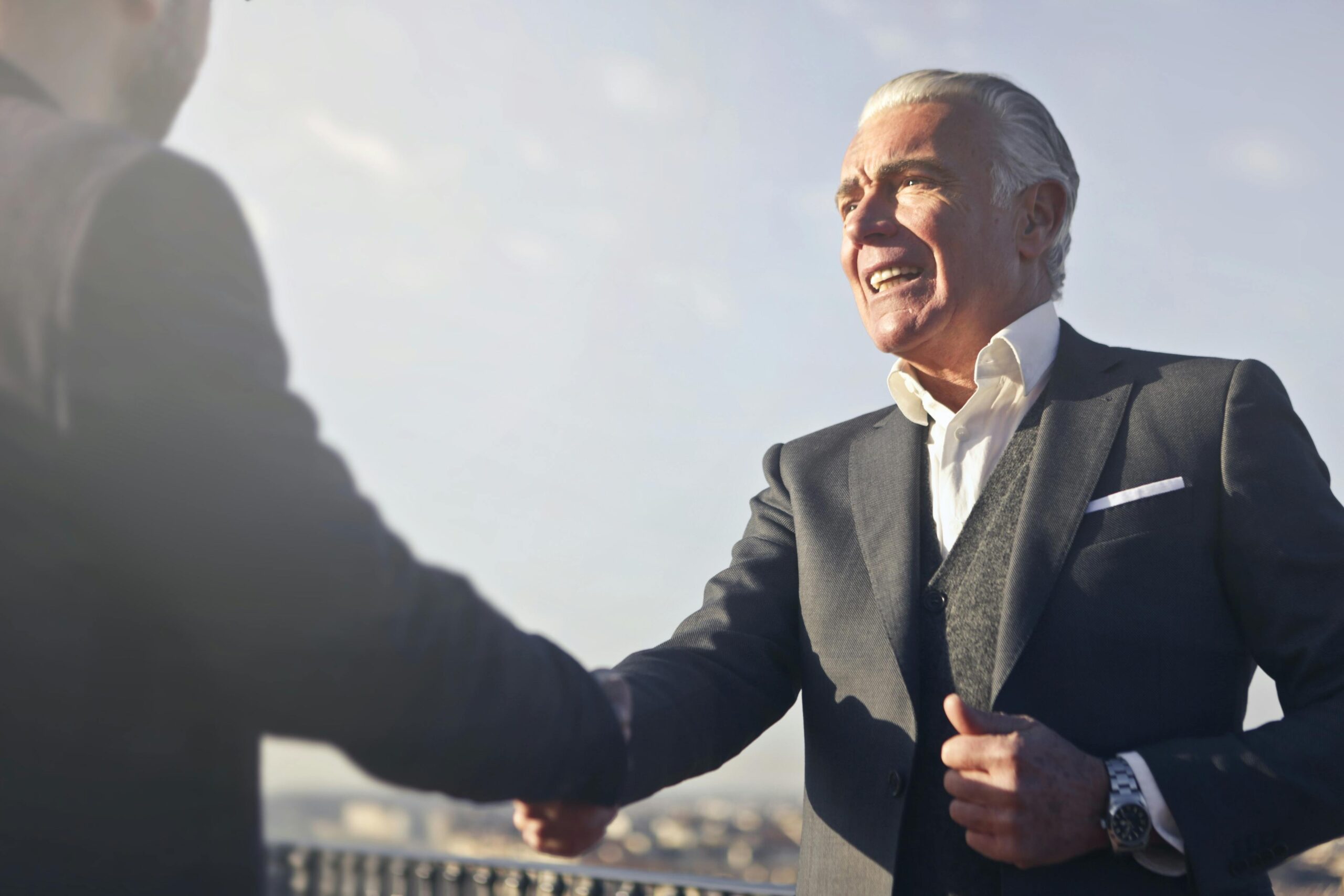 A senior businessman warmly shakes hands outdoors, symbolizing agreement and mutual respect.